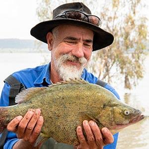 Person standing outdoors, smiling and holding a native fish